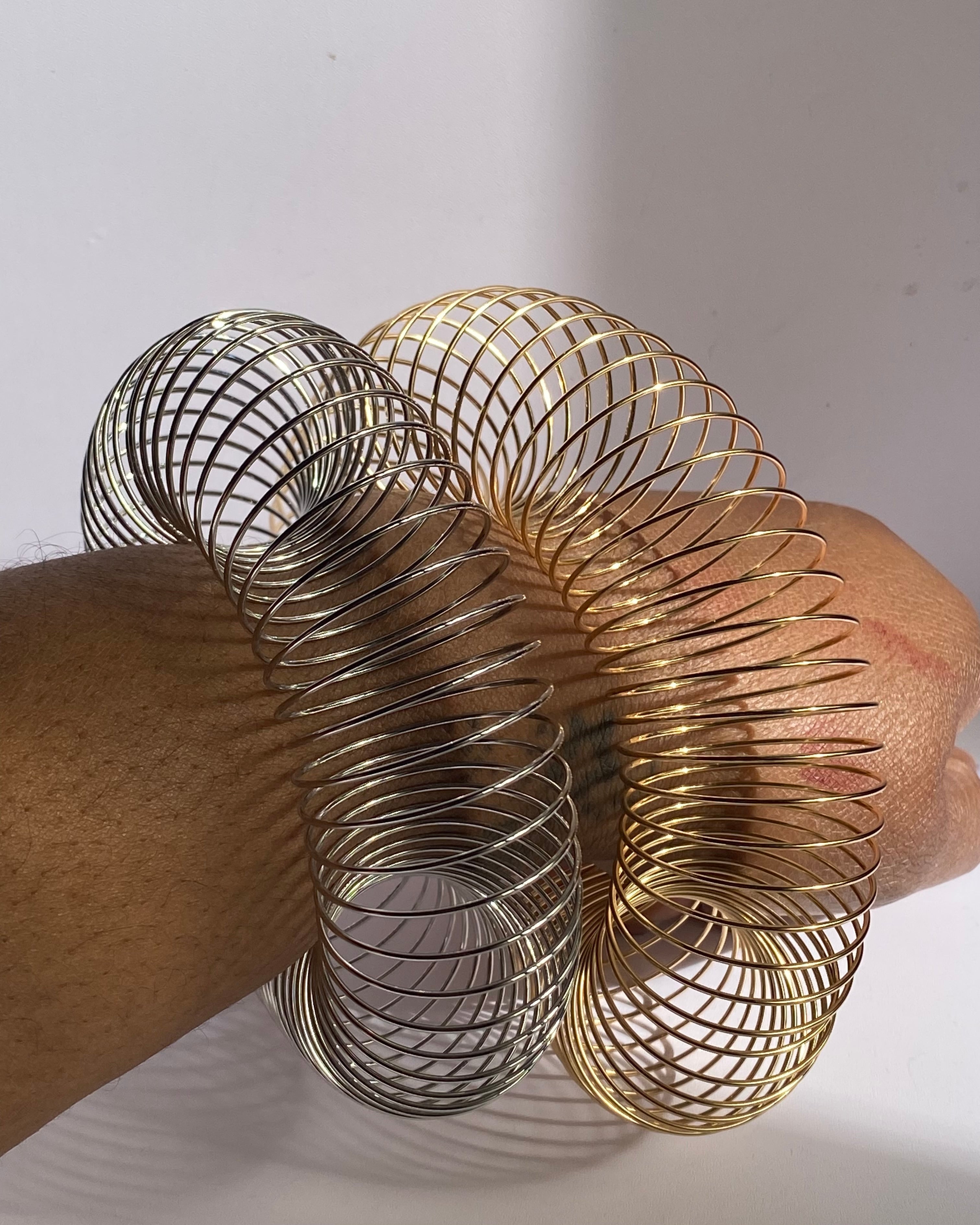 Gold and silver expandable wire cuff bracelets worn on wrist showing open statement style