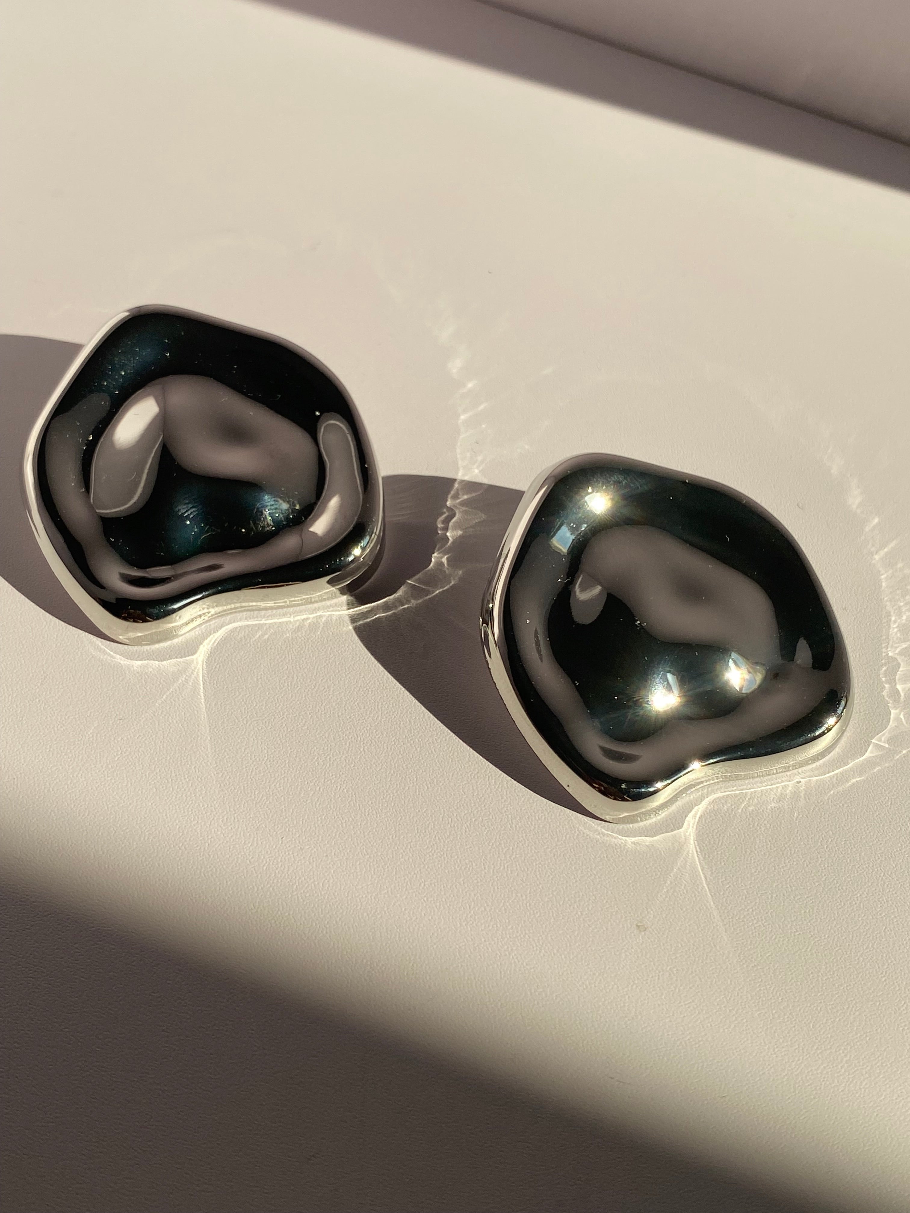 Oversized silver rounded square statement stud earrings with smooth sculptural design and reflective metallic finish