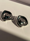 Oversized silver rounded square statement stud earrings with smooth sculptural design and reflective metallic finish