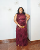 Woman wearing burgundy sequin maxi gown with layered chiffon skirt and gold accessories