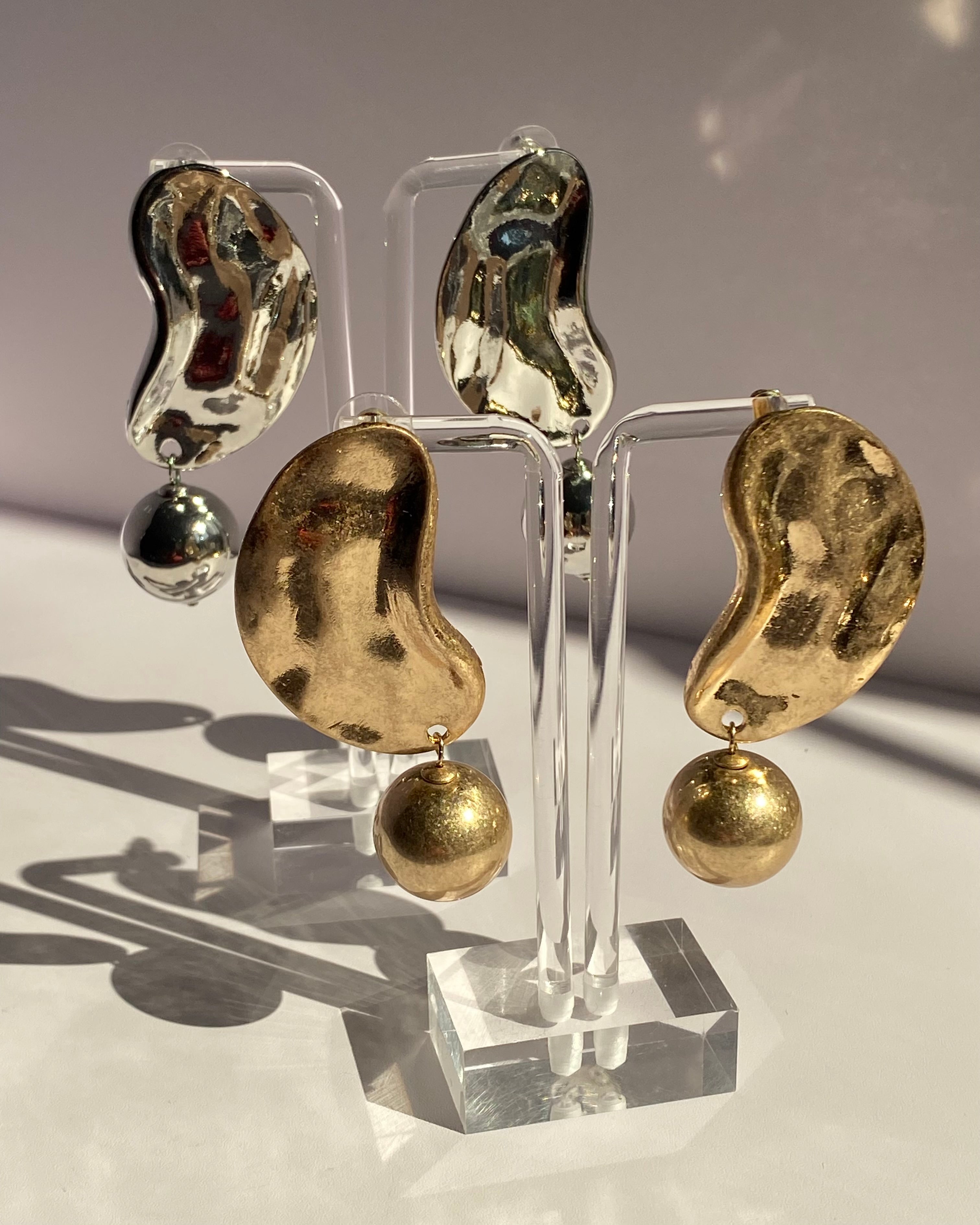 Gold and silver sculpted wave statement earrings with textured abstract design and dangling metallic ball