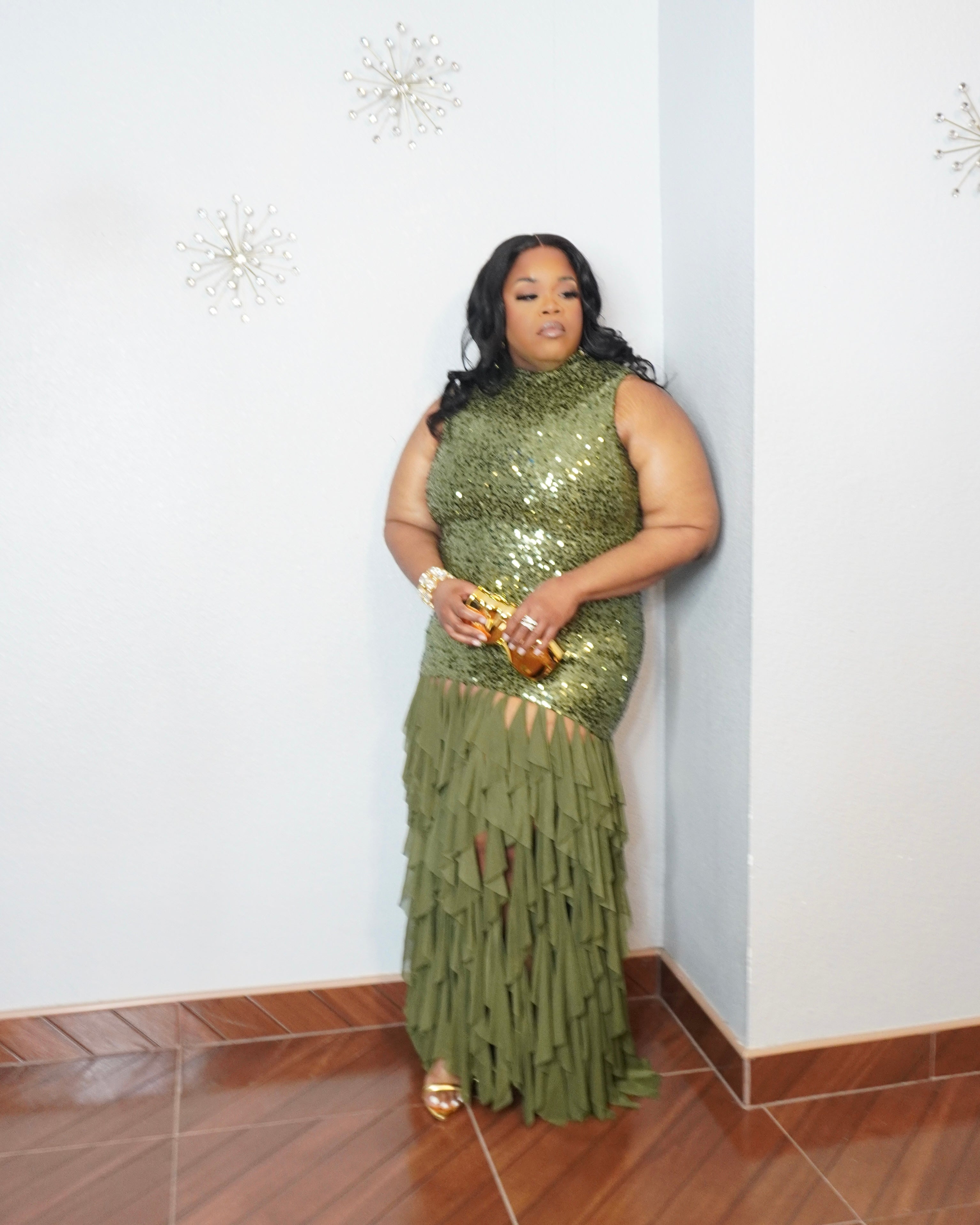 Model posing in olive green sequin evening gown with gold accessories