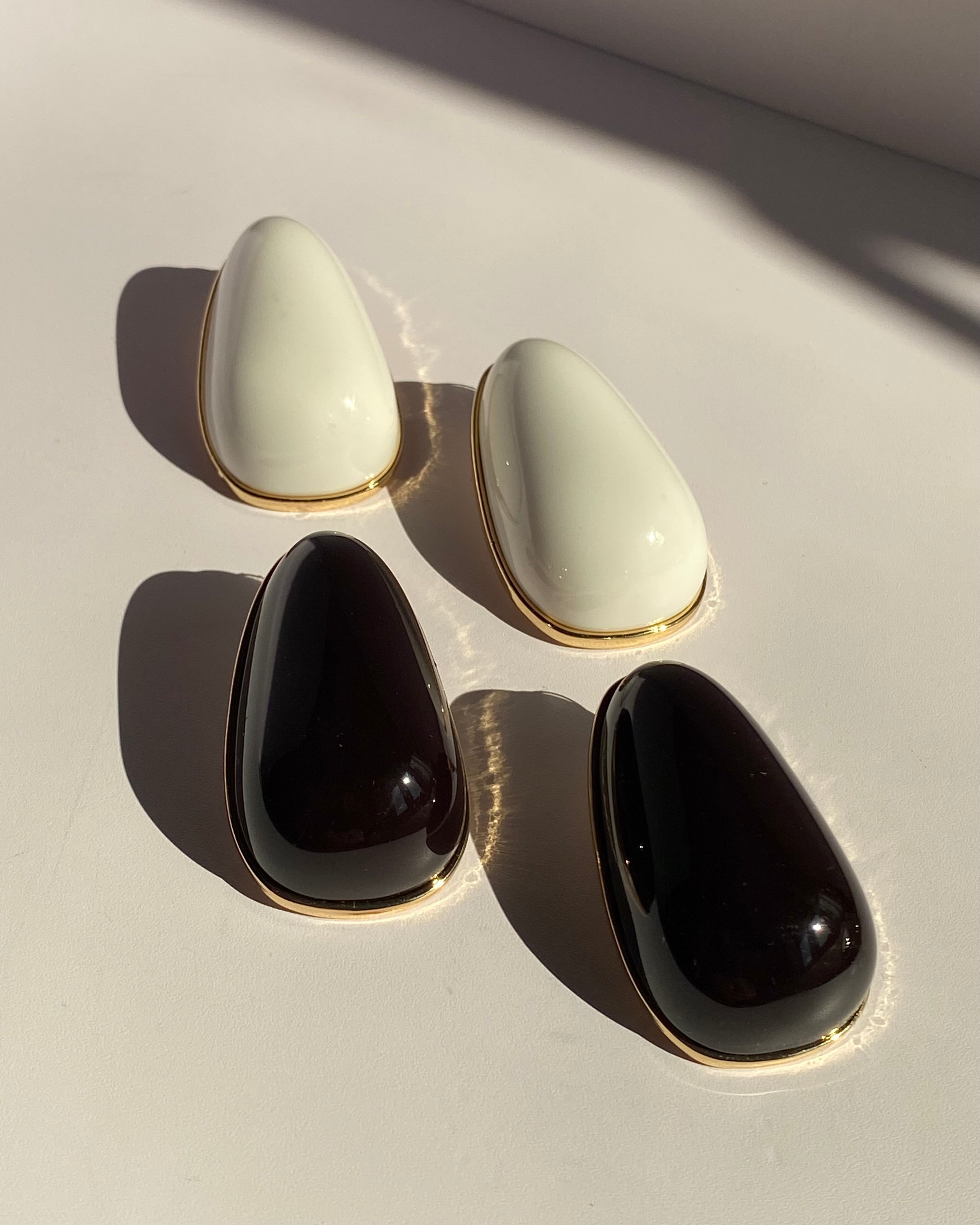 Black sculptural teardrop stud earrings with polished gold-tone border displayed on clear jewelry stand