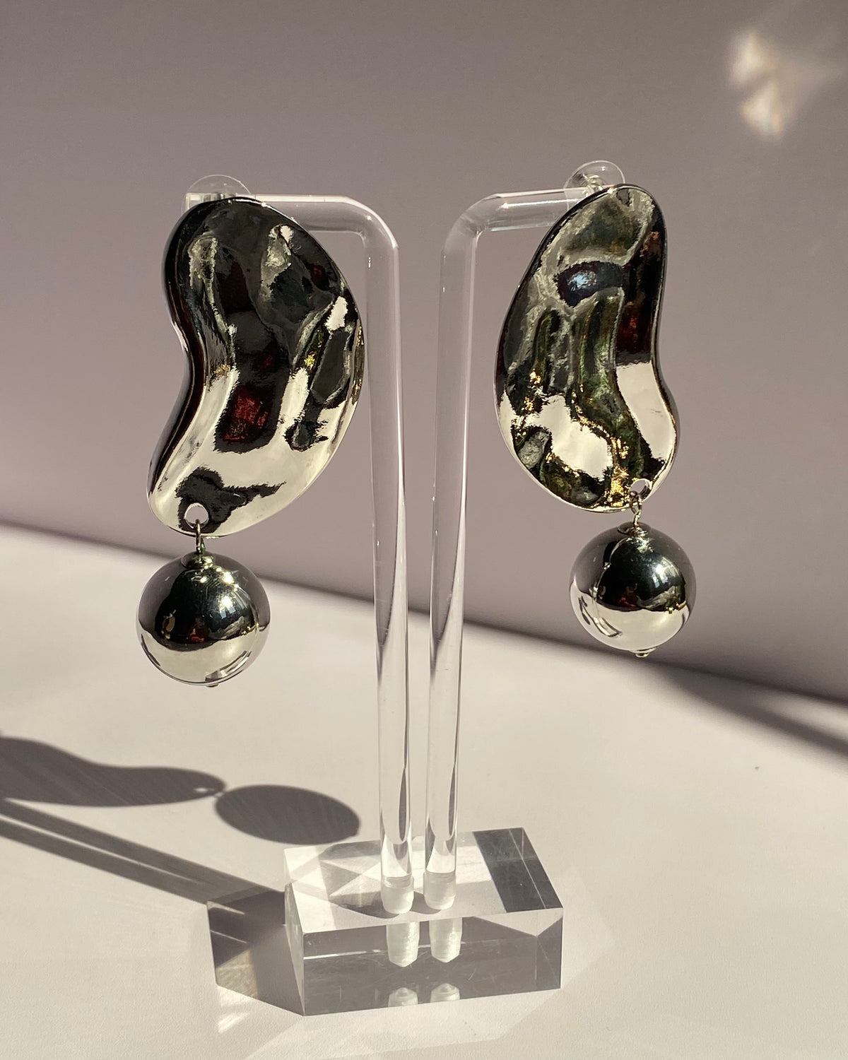 Silver sculpted wave statement drop earrings featuring an abstract metallic design and dangling silver ball