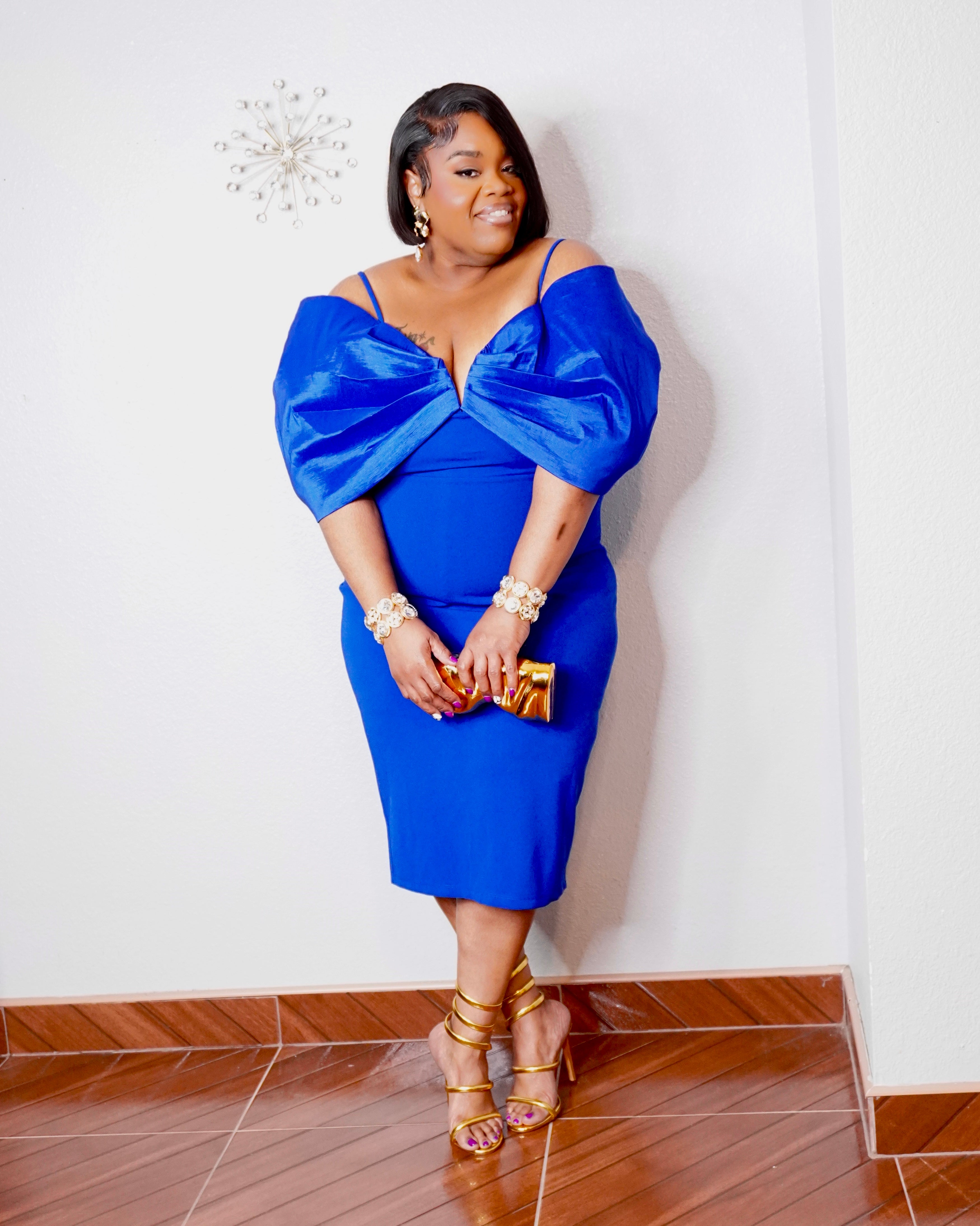 LYSAIRE royal blue plus size off-shoulder midi dress with dramatic draped sleeves, fitted silhouette, gold heels and matching clutch.