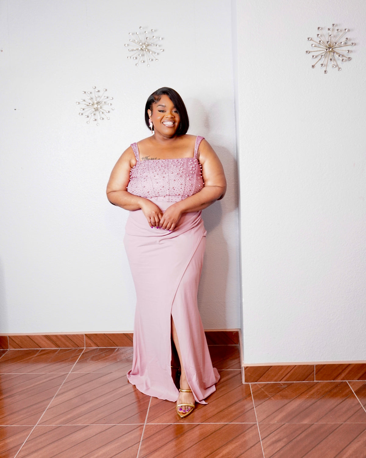 Plus size model wearing the LYSAIRE Rosé Royale dusty pink pearl embellished formal maxi dress, featuring a sparkling rhinestone and pearl-adorned square neckline, delicate shoulder straps, fitted waist, flowing floor-length skirt, and elegant front thigh-high slit, styled with metallic gold heels.