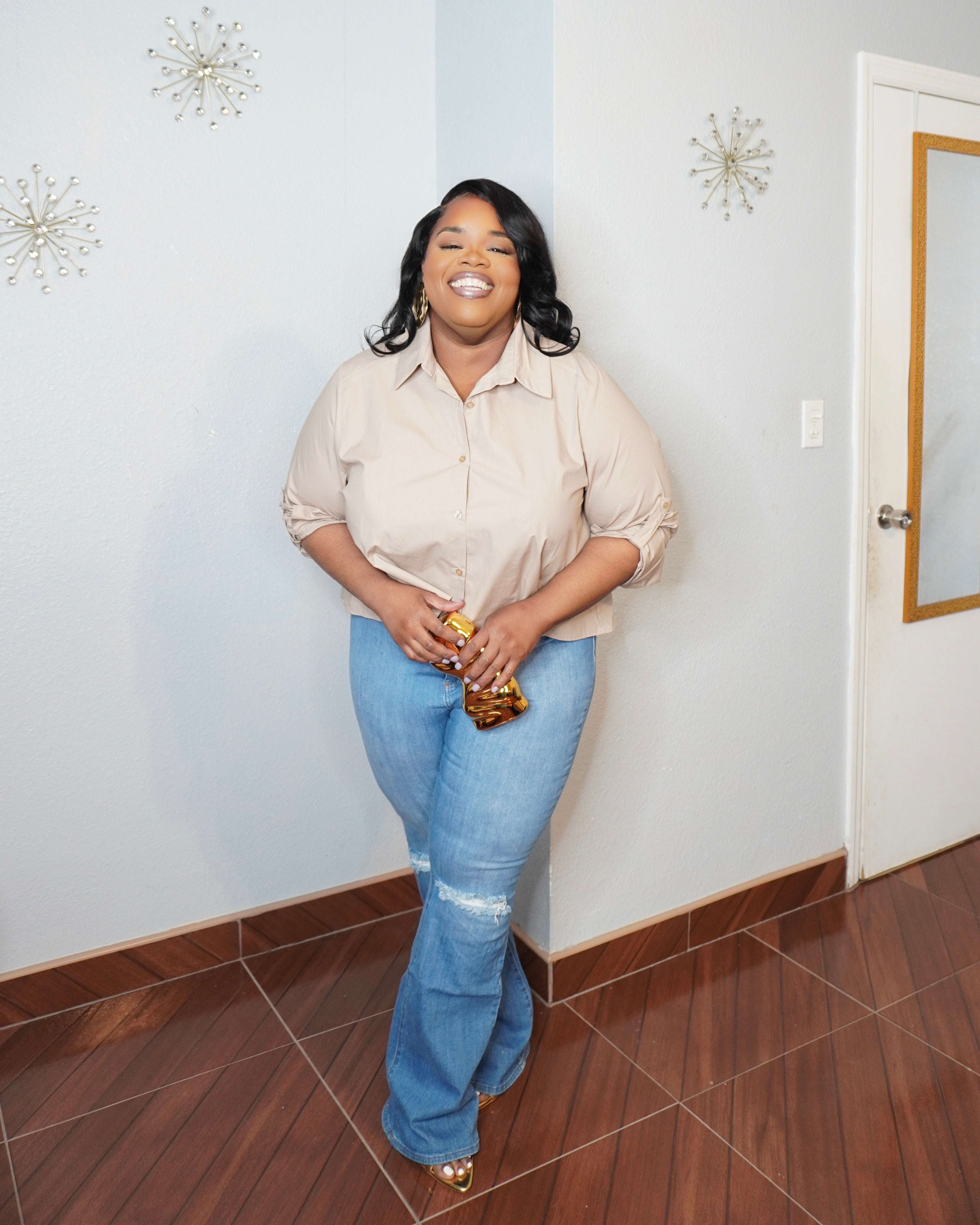 Plus size model smiling in beige pleated back blouse styled with jeans and heels
