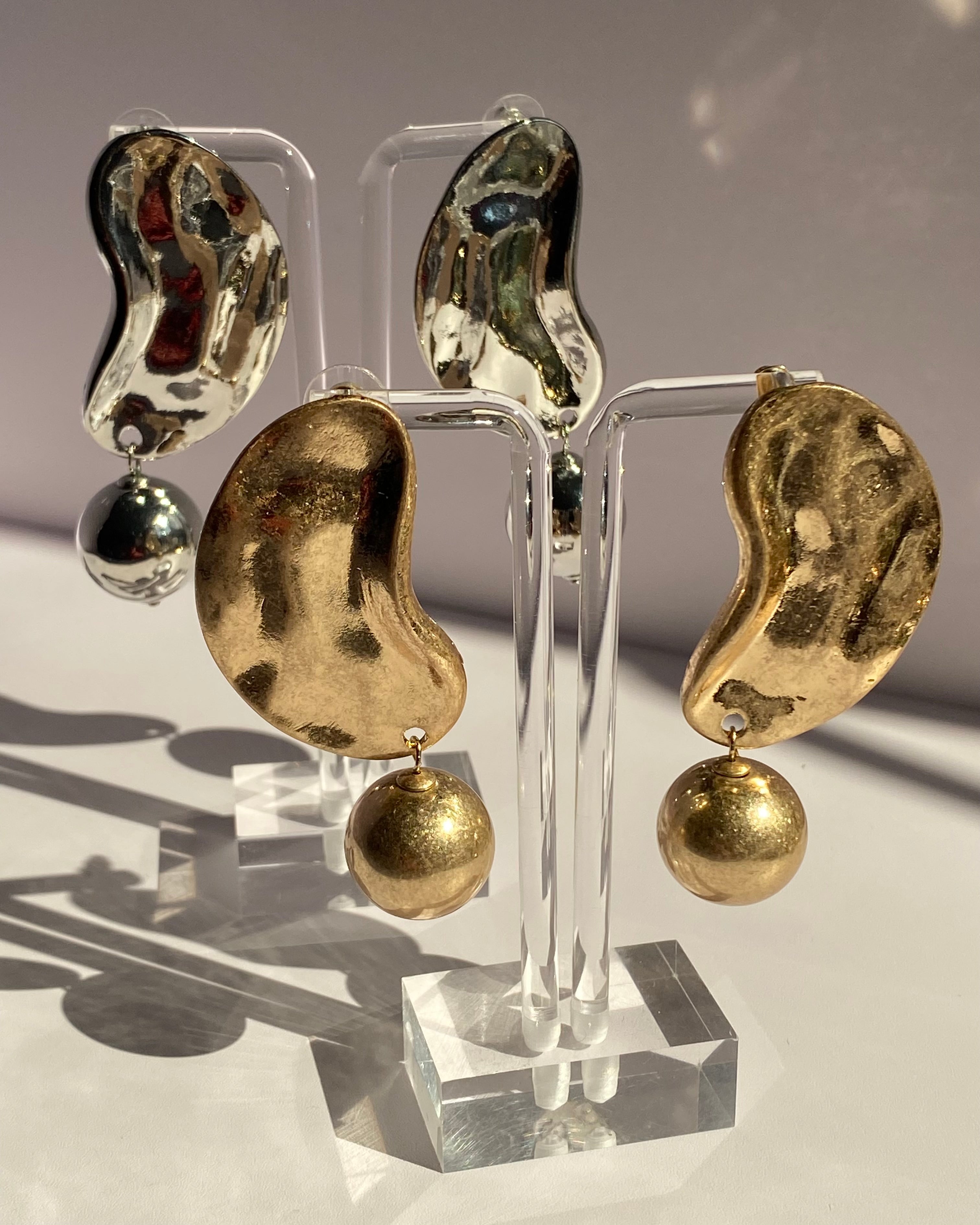 Gold and silver sculpted wave statement earrings with textured abstract design and dangling metallic ball