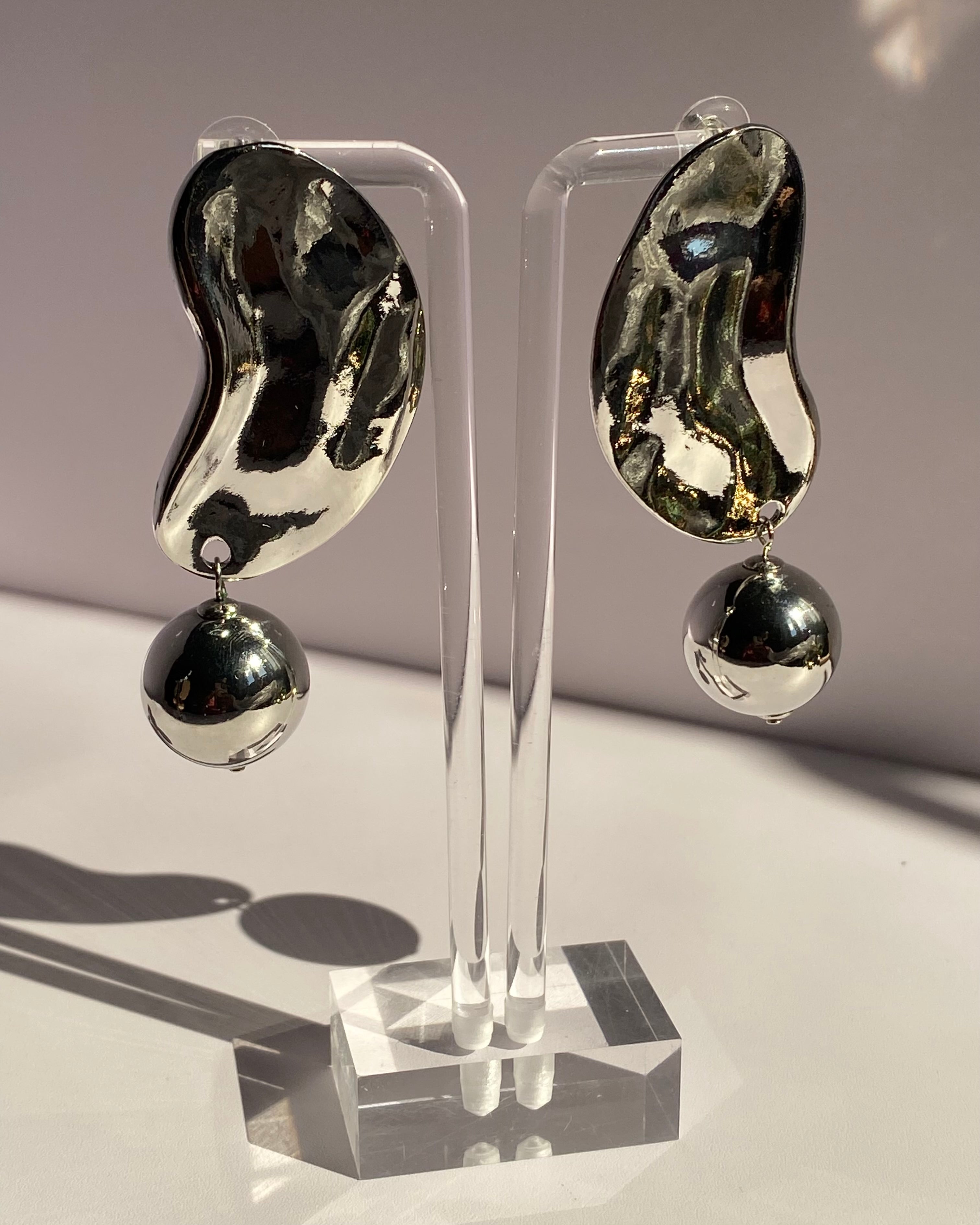 Silver sculpted wave statement drop earrings featuring an abstract metallic design and dangling silver ball