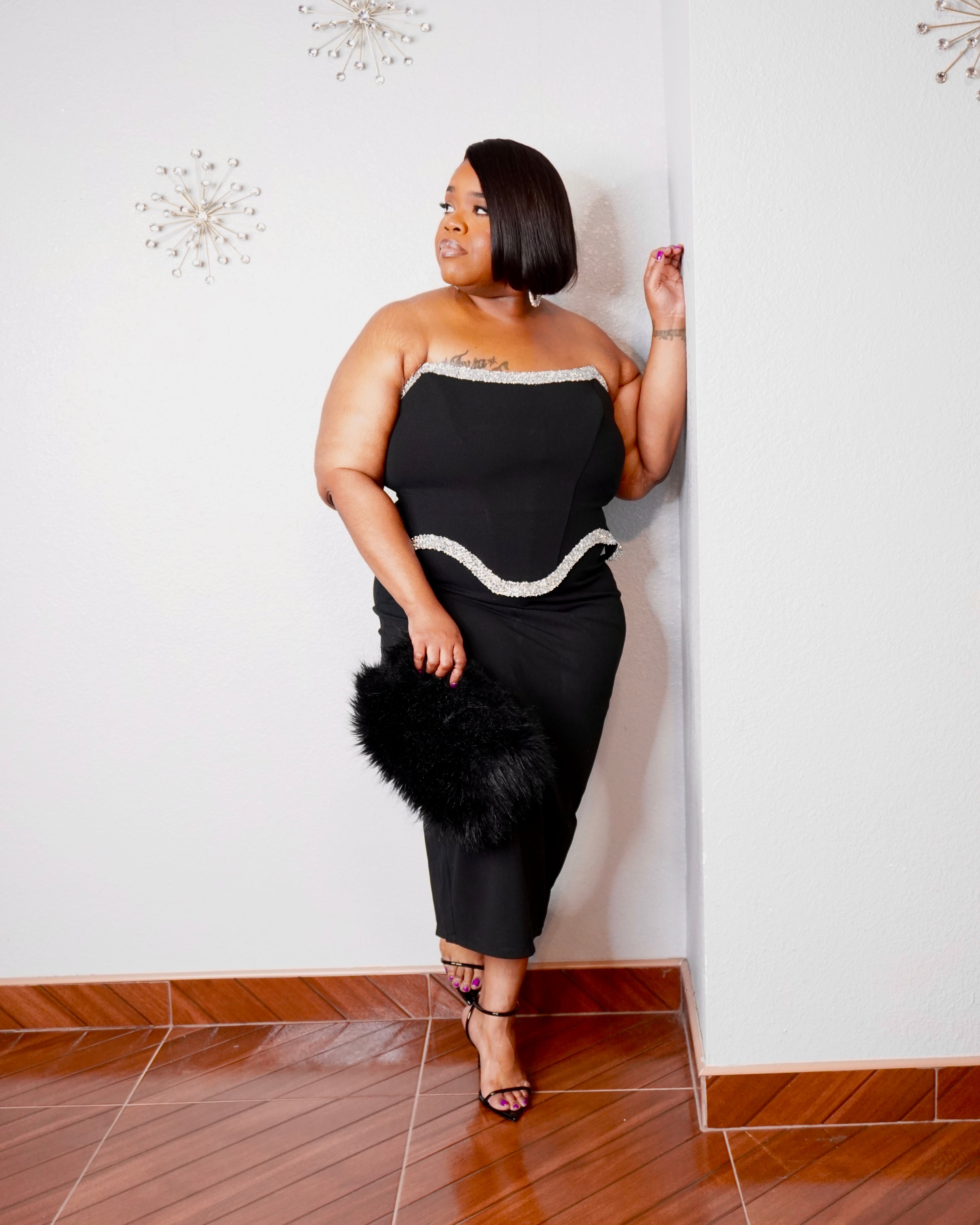 LYSAIRE elegant black strapless midi dress styled with black heels and a statement faux-fur handbag.