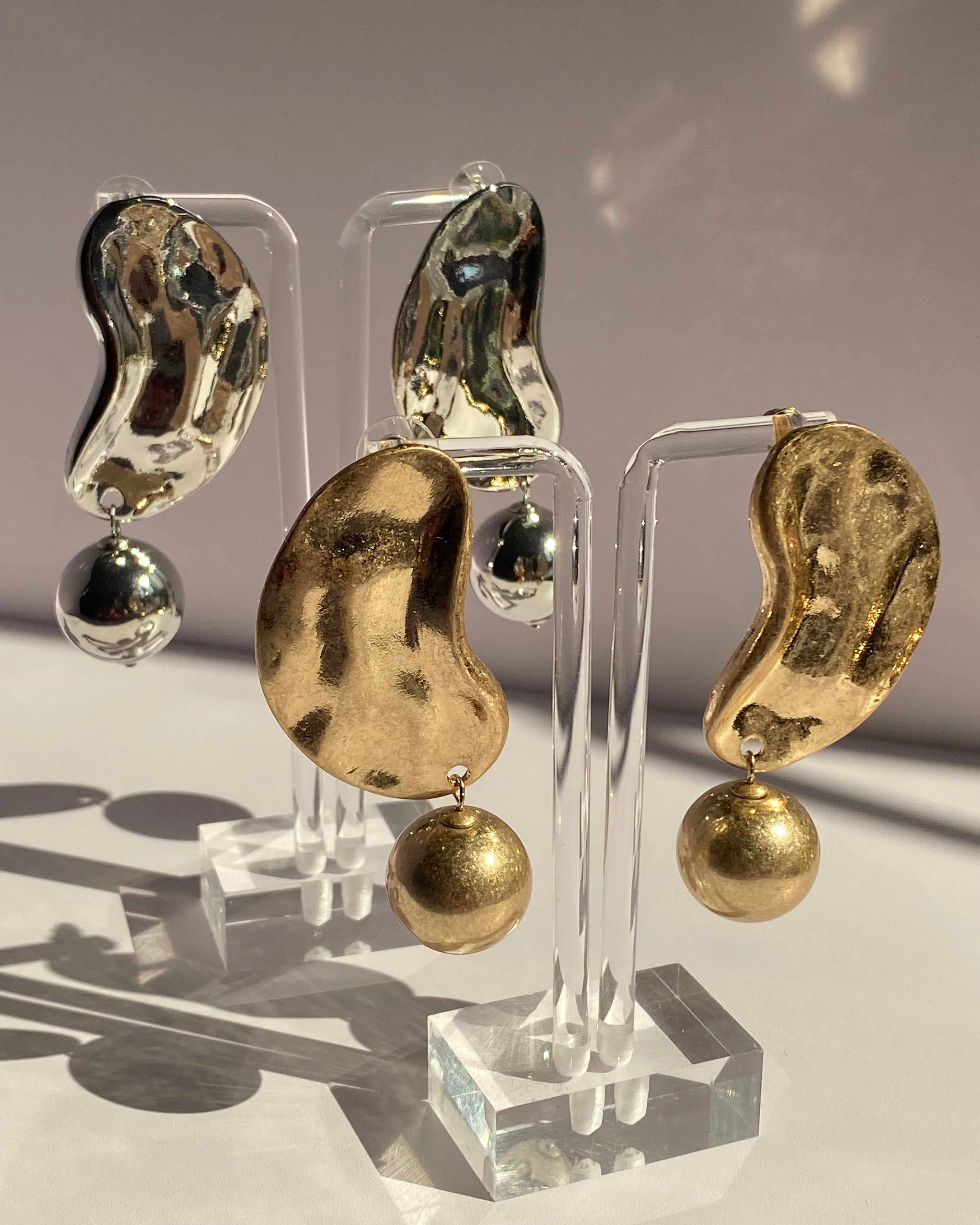 Gold and silver sculpted wave statement earrings with textured abstract design and dangling metallic ball